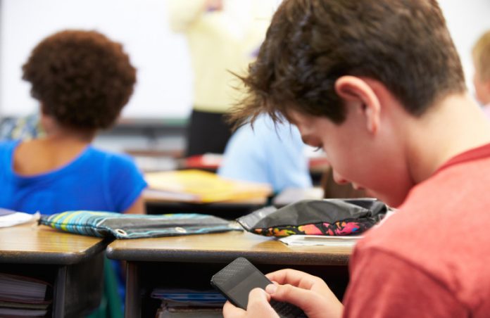 Pupil Sending Text Message On Mobile Phone In Class